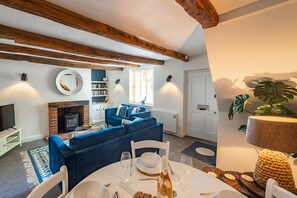 A cozy living room with a fireplace, blue sofa, dining table set, and a large plant.