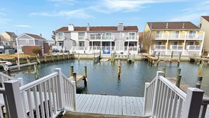 Una propiedad frente al agua con un muelle de madera que conduce a un puerto deportivo, rodeada de edificios de varios pisos con balcones.