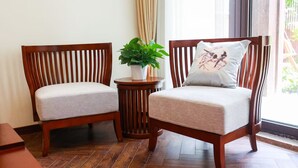 Two wooden chairs with cushioned seats and backs, a small round wooden table with a potted plant, and a window with curtains. - Book and Bed-Chong Ming (Shanghai)