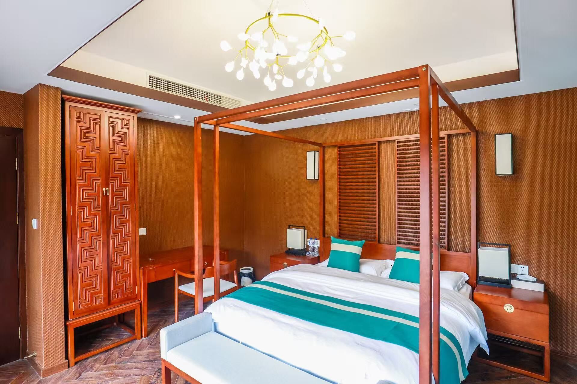 A four-poster bed with a canopy, a wooden wardrobe, a desk with a chair, and a bedside table with a lamp.