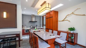 A modern kitchen with a central island, wooden cabinetry, and a dining area with a long table and chairs. - Book and Bed-Chong Ming (Shanghai)