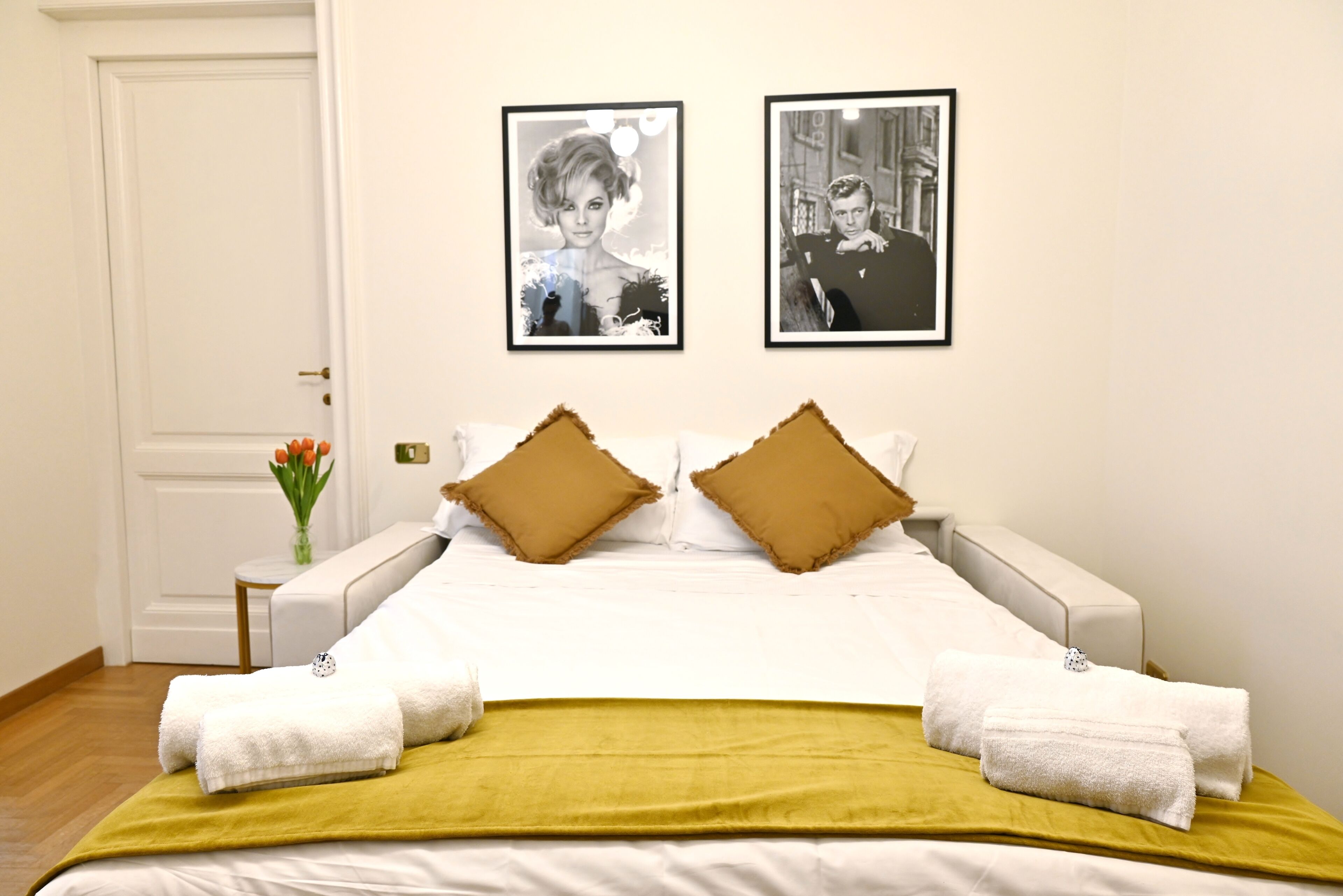 A hotel room with a bed, two pillows, a green throw, and two towels.