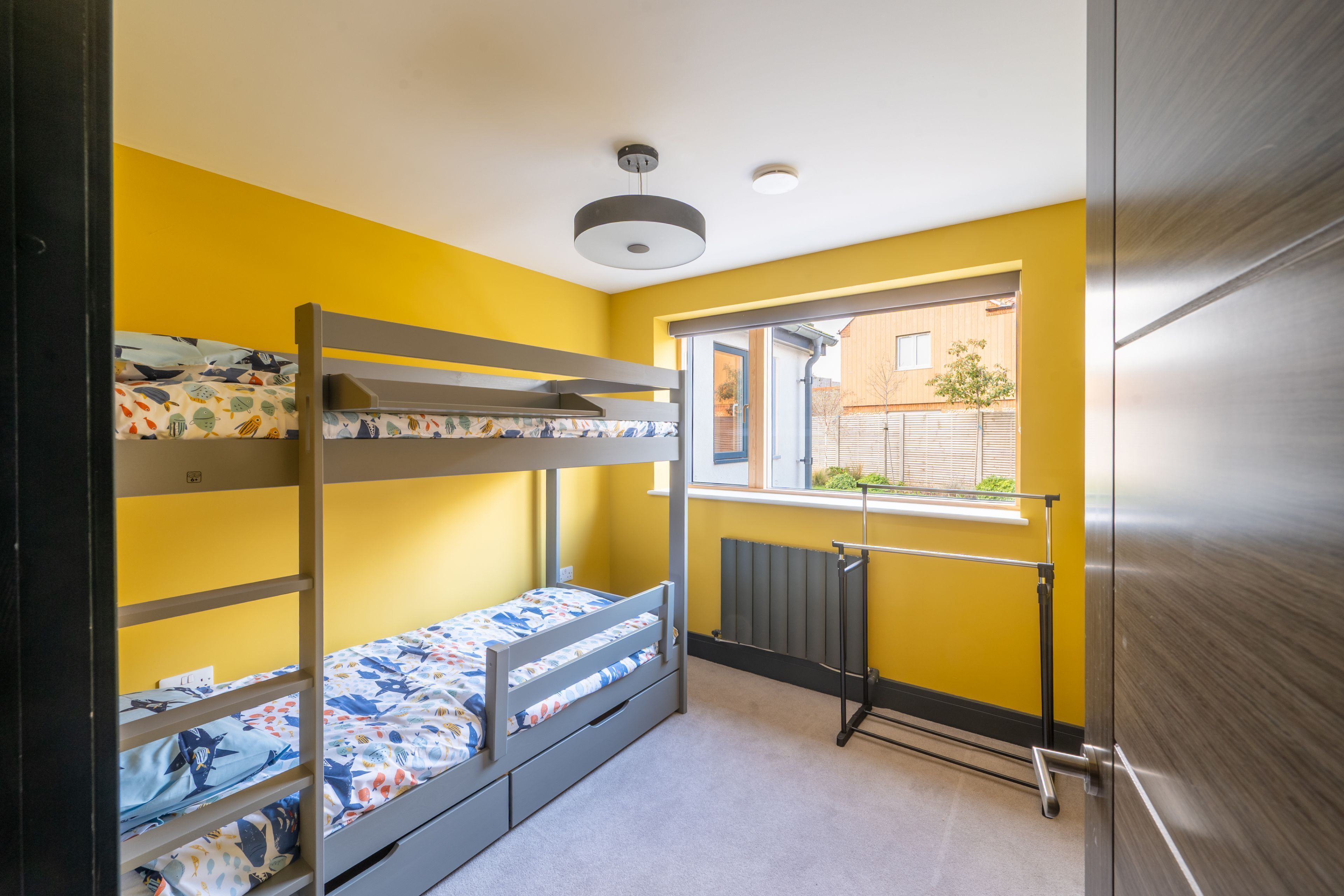A bunk bed room with a window, a radiator, and a door.