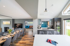 A modern kitchen with a central island, a dining area with a long table, and a living area with a sofa and TV. - Hungate Lodge, Old Hunstanton, Norfolk (Old Hunstanton)