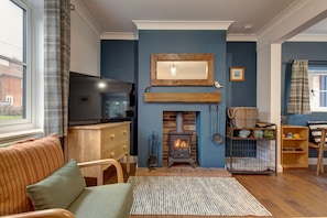 A cozy living room with a fireplace, a television, and a comfortable seating area. - 1 The Cottages, Aylmerton, Norfolk (Aylmerton)