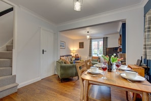 A dining area with a wooden table set for four, a sofa, and a staircase. - 1 The Cottages, Aylmerton, Norfolk (Aylmerton)