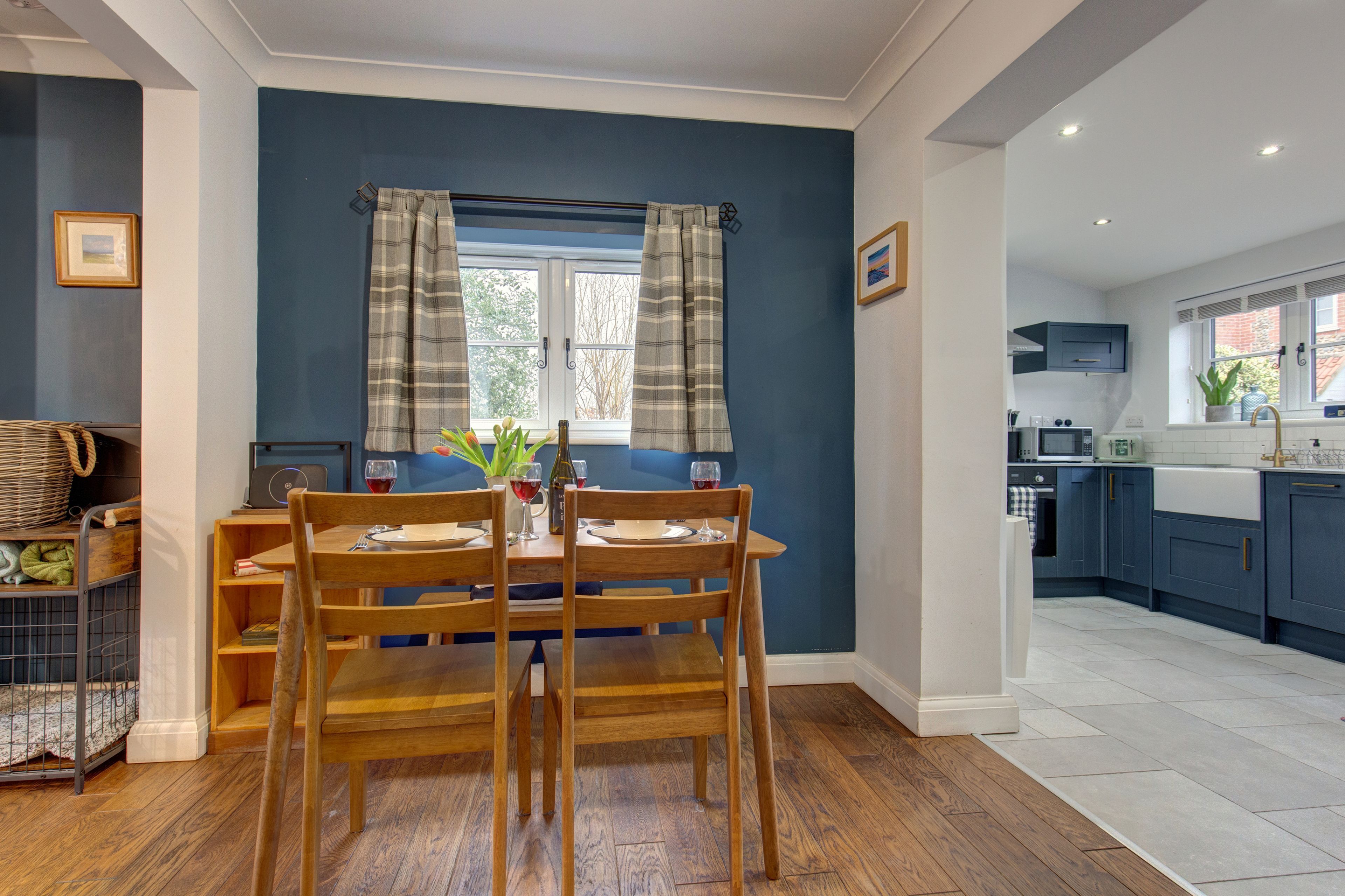 A dining area with a table and chairs, a window with curtains, a kitchen with cabinets, and a white sink.