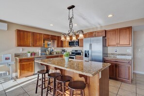 A kitchen with wooden cabinets, a granite countertop, a stainless steel refrigerator, and a bar stool area.