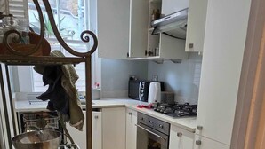 A kitchen with white cabinets, a stove, an oven, and a metal rack with kitchen utensils. - 2-bed Garden Flat in Fulham (London)