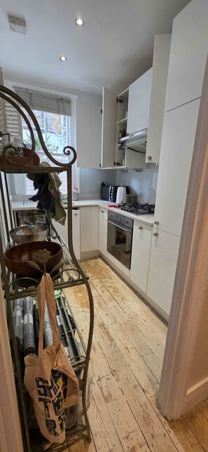 A kitchen with white cabinets, a stove, an oven, and a metal rack with kitchen utensils. - 2-bed Garden Flat in Fulham (London)
