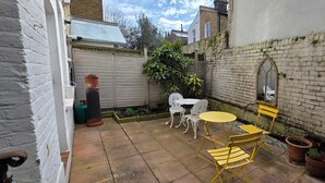 A patio with a table and chairs, a brick wall, and a white fence. - 2-bed Garden Flat in Fulham (London)