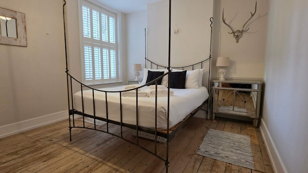 A bedroom with a four-poster bed, a bedside table with a lamp, a mirror, and a wall-mounted deer head decoration. - 2-bed Garden Flat in Fulham (London)