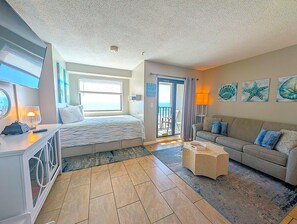 A bedroom with a bed, a desk, a dresser, a balcony, a sofa, and artwork on the walls. - Oceanfront Condo | Myrtle Beach Resort RT0703 (Myrtle Beach)