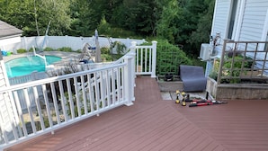 Une terrasse en bois avec une piscine, une balustrade blanche et un espace jardin.