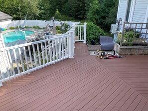 A wooden deck with a pool, white railing, and a garden area. - Meadow Lane -Bar and Pool (Ogunquit)