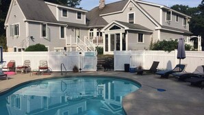 Une maison à deux étages avec une piscine, une clôture blanche en bois et un espace salon extérieur.