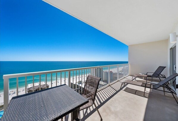 Un balcon avec vue sur la plage et l’océan, une table et deux chaises.