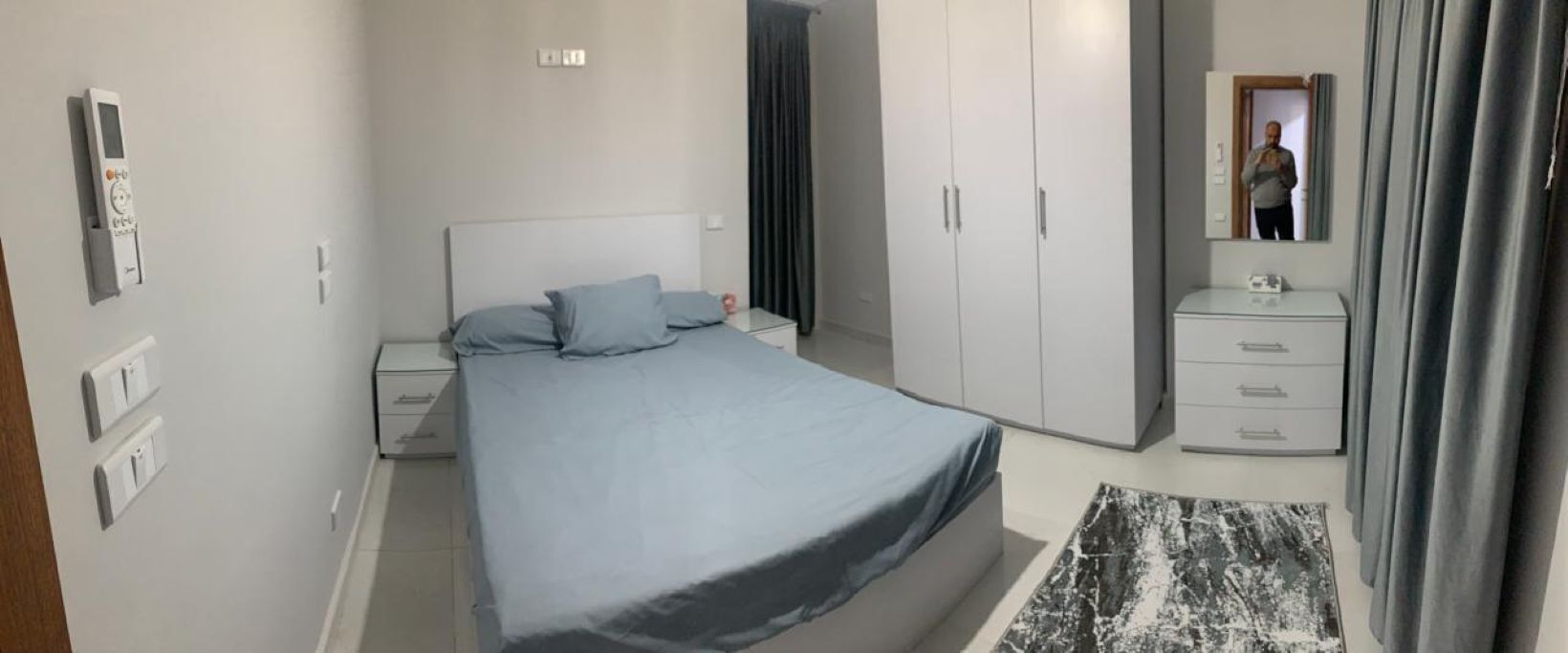 A bedroom with a bed, a nightstand, a dresser, a mirror, and a wardrobe.