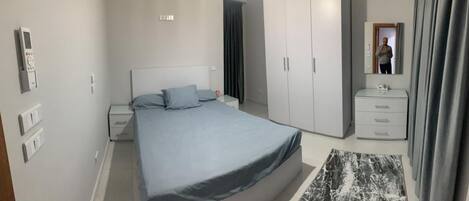 A bedroom with a bed, a nightstand, a dresser, a mirror, and a wardrobe.