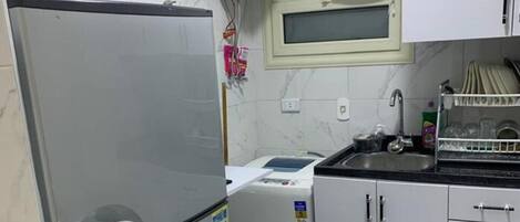 A kitchen with a stainless steel refrigerator, a microwave, a sink, and a window with an air conditioner.