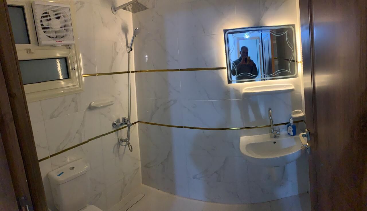 A bathroom with a shower, toilet, sink, and a mirror with a reflection.