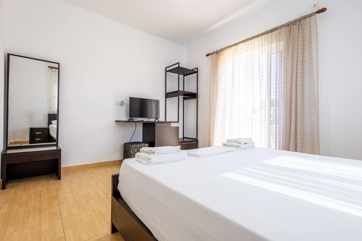 Une chambre d’hôtel avec un lit, une télévision, une étagère et un miroir.