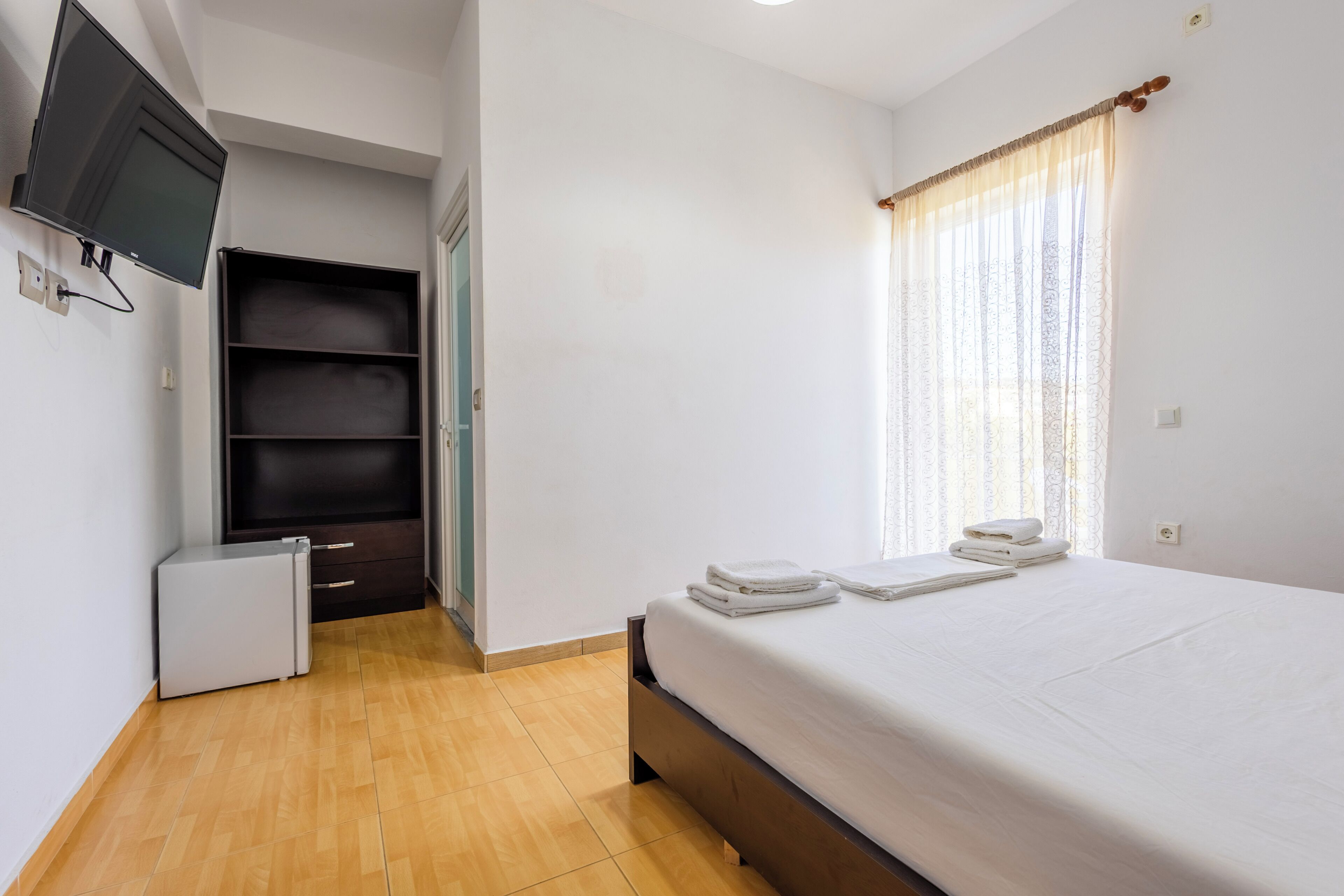 A bedroom with a bed, a TV, a wardrobe, and a window with curtains.