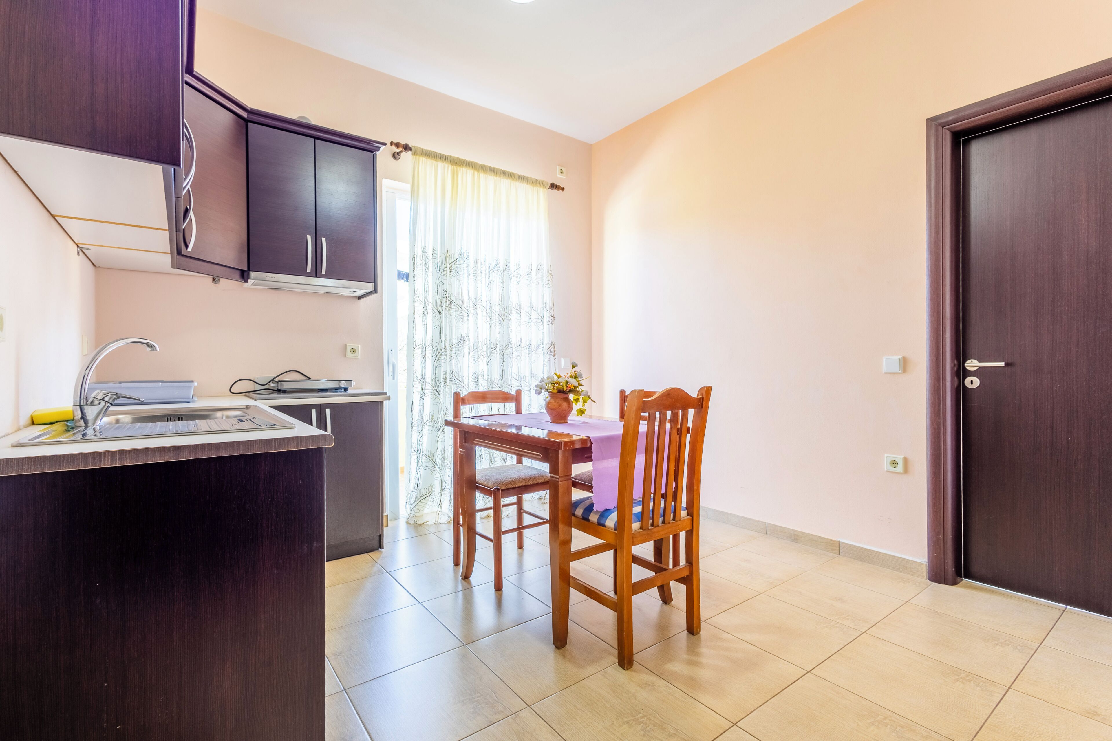 A kitchen with a sink, cabinets, and a dining table with chairs.