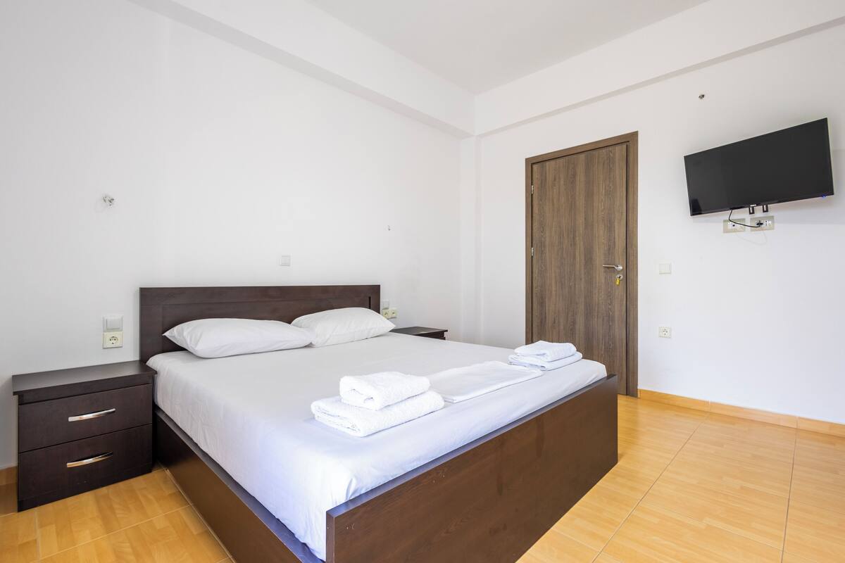 Une chambre moderne avec un lit en bois, du linge de lit blanc, un téléviseur à écran plat et une porte en bois.