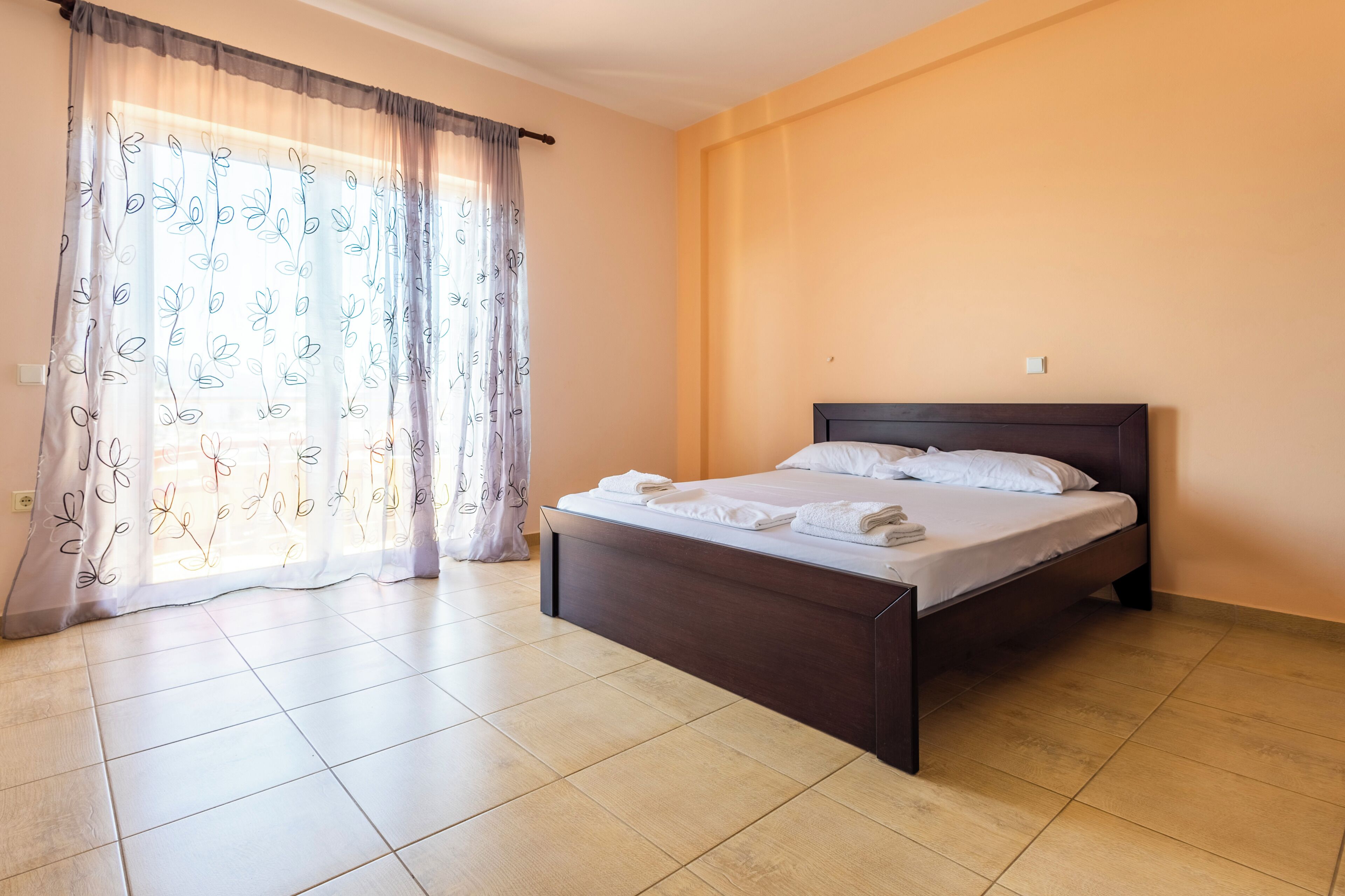 A bedroom with a bed, curtains, and a tiled floor.