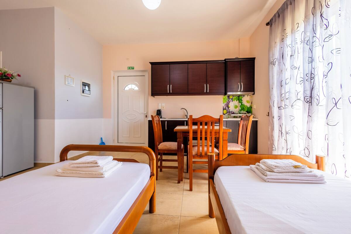 Une chambre d’hôtel avec deux lits, un bureau, une chaise, un coin cuisine et une salle de bain.