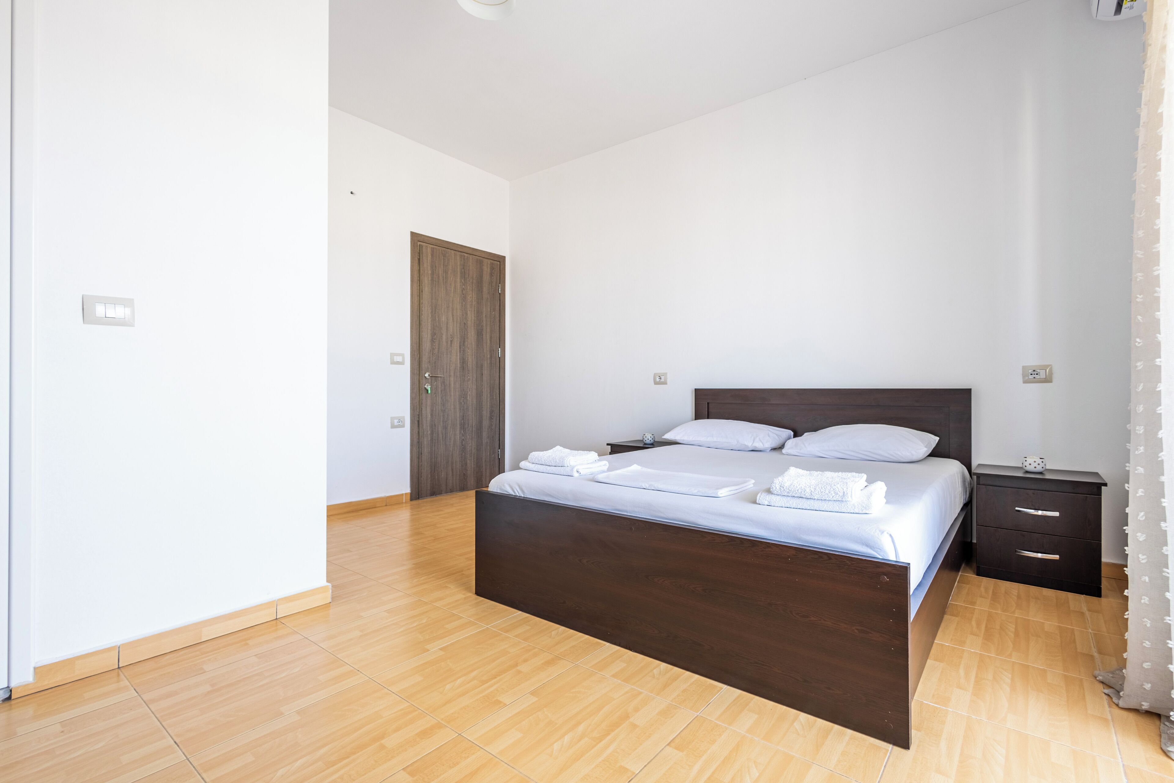 Ein Schlafzimmer mit einem hölzernen Bett, einem Nachttisch, einer Tür und einem Lichtschalter.