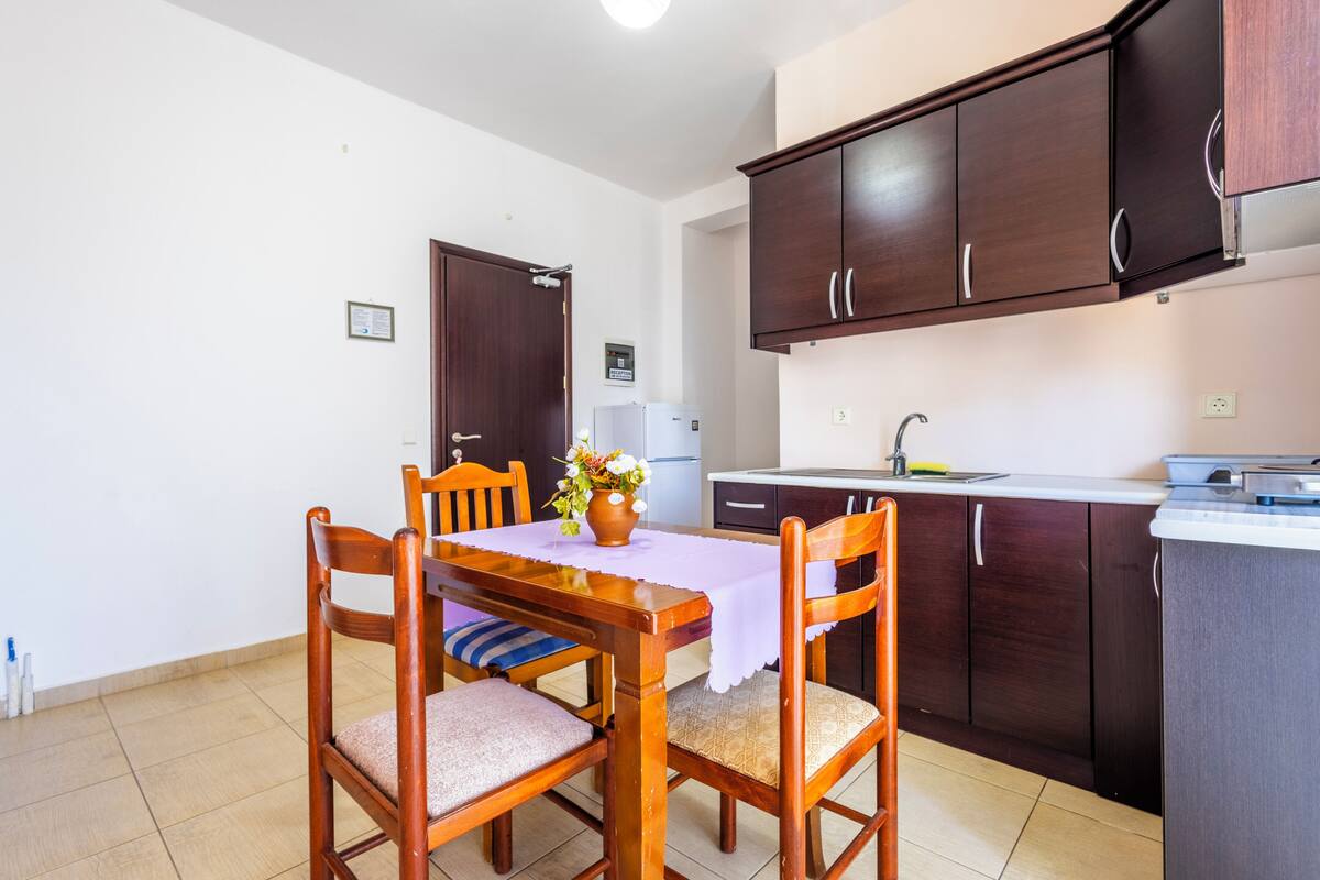 Un coin repas avec des chaises et une table en bois, une cuisine avec des meubles en bois foncé et un réfrigérateur blanc.