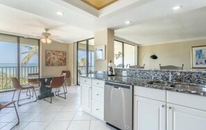 A modern kitchen with a granite countertop, stainless steel appliances, and a dining area with chairs and a table. - Condo on Naples Vanderbilt Beach close to the Ritz Carlton and LaPlaya Hotels. (Naples)