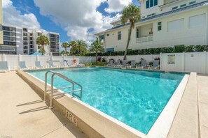 Une piscine avec des chaises longues, une clôture et un bâtiment en arrière-plan.