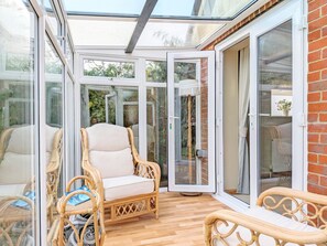 Una veranda con mobili in vimini, una porta in vetro e vista sul verde.