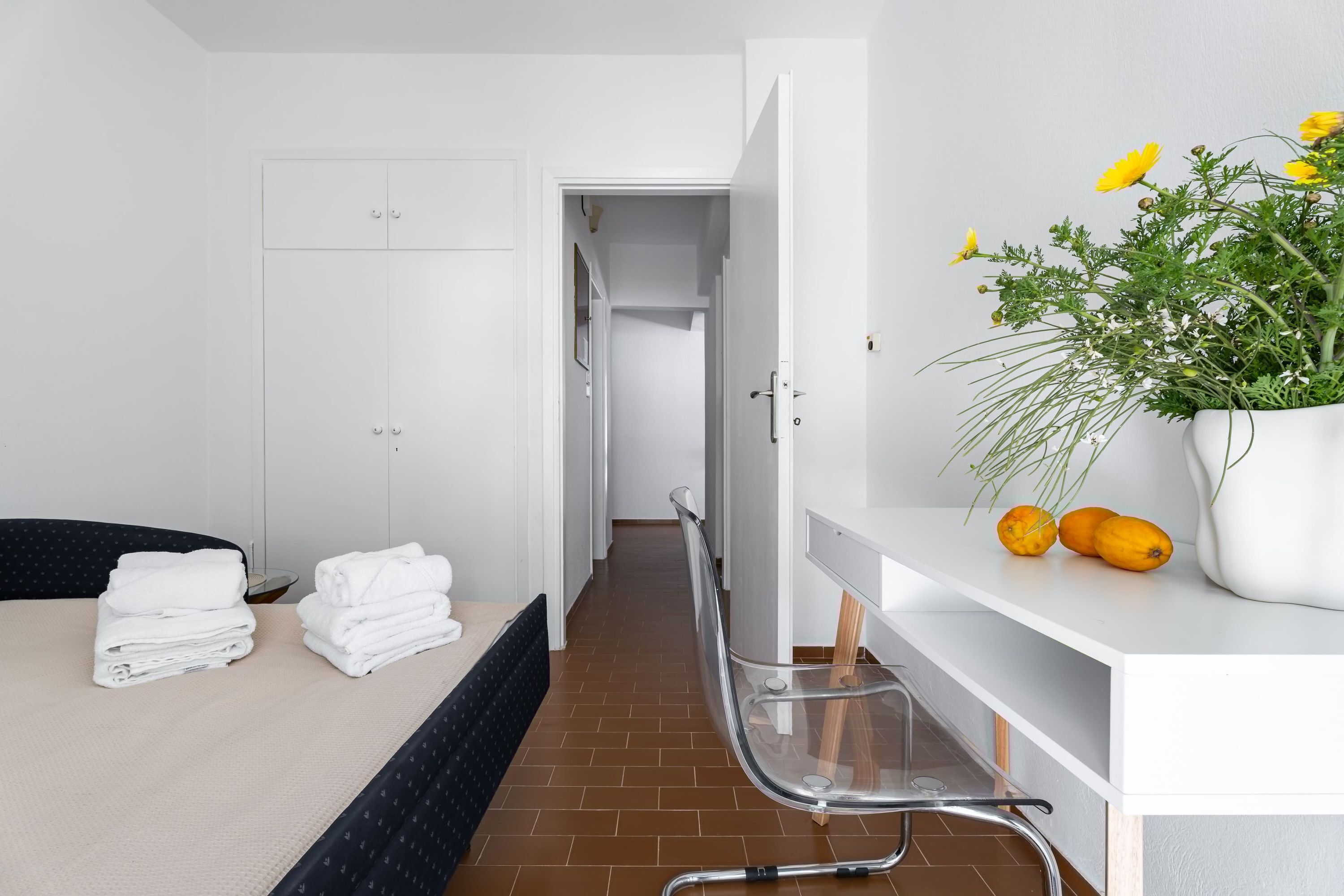 Une chambre d’hôtel avec un lit, une chaise, un bureau agrémenté d’une plante et une porte donnant sur une autre pièce.