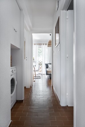 A hallway with a washing machine, a bed, and a chair. - Saronida Coastal Escape | 2BR Apartment (Saronida)