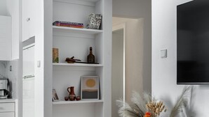 Een modern interieur met een witte schapjes, een flatscreen televisie aan de muur en een tafeltje met een vaas gedroogde bloemen.