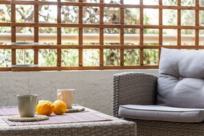 A wicker sofa with cushions, a table with a placemat, and two cups and lemons on the table. - Saronida Coastal Escape | 2BR Apartment (Saronida)