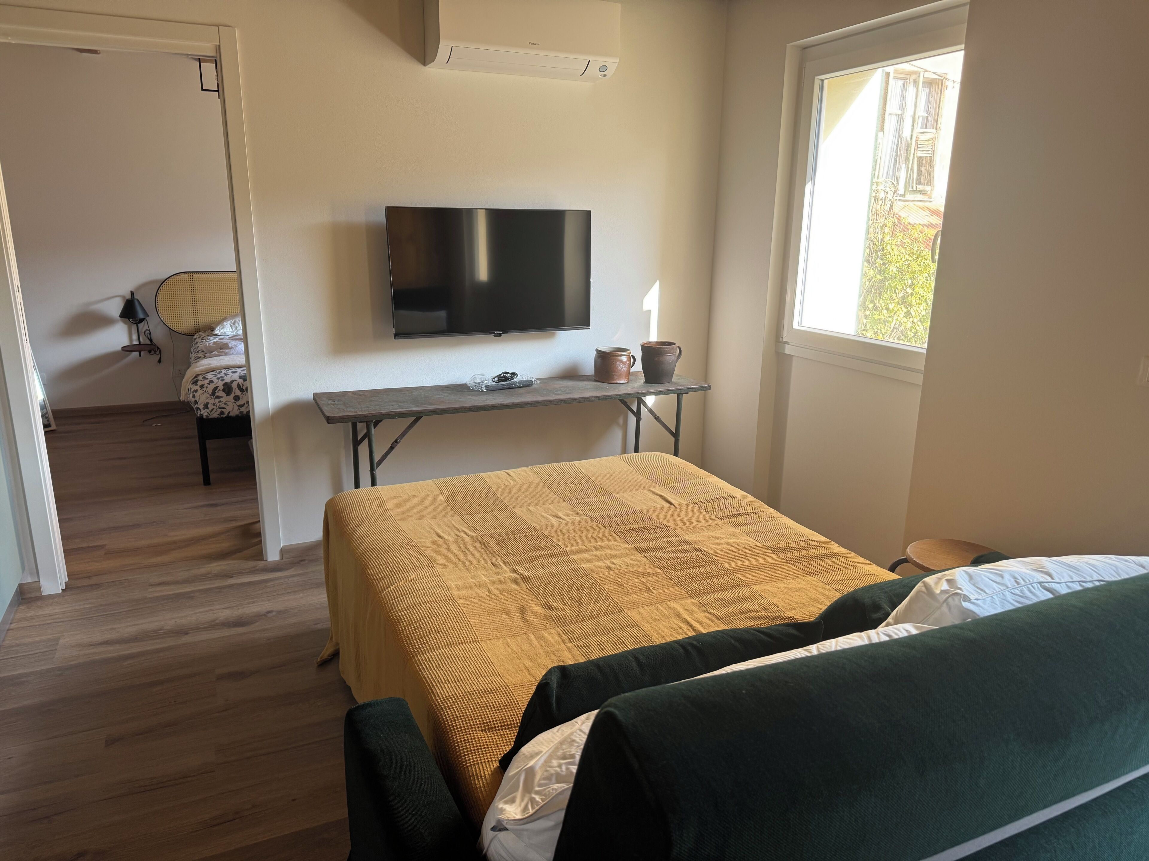 A room with a bed, a TV, a table with two mugs, and a window.