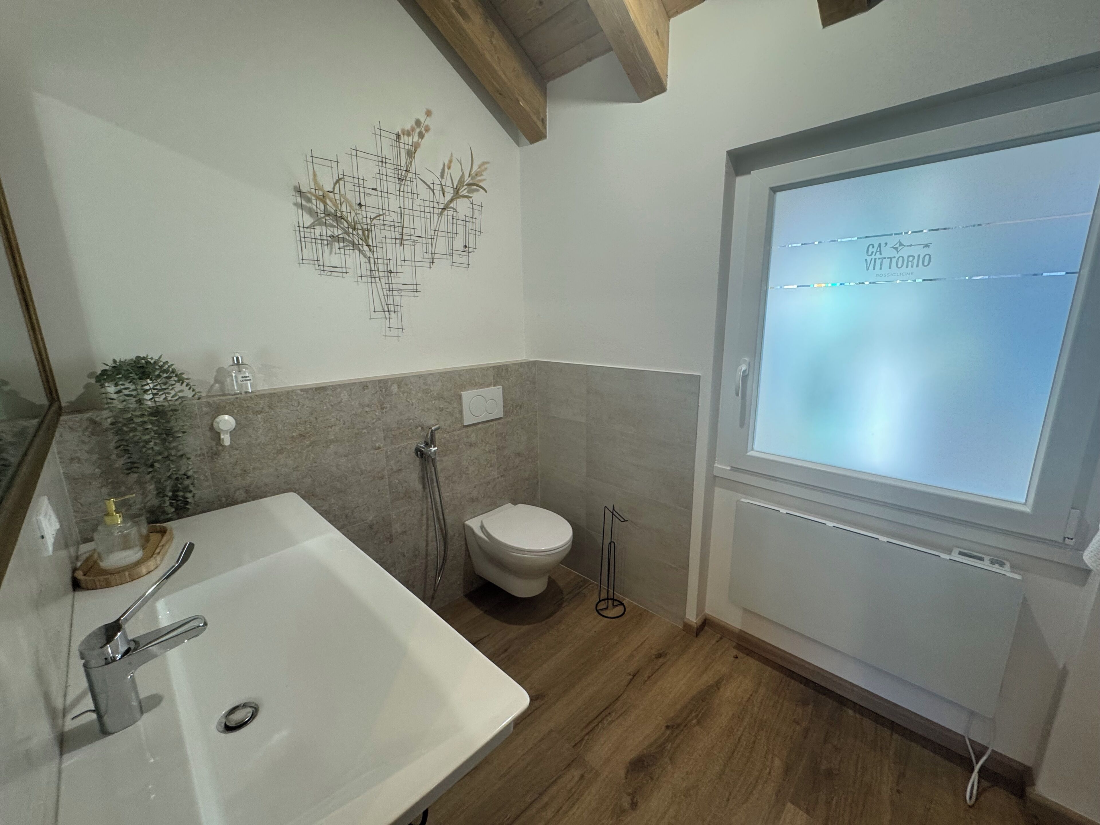 A modern bathroom with a sink, toilet, shower, and a window with a frosted glass.