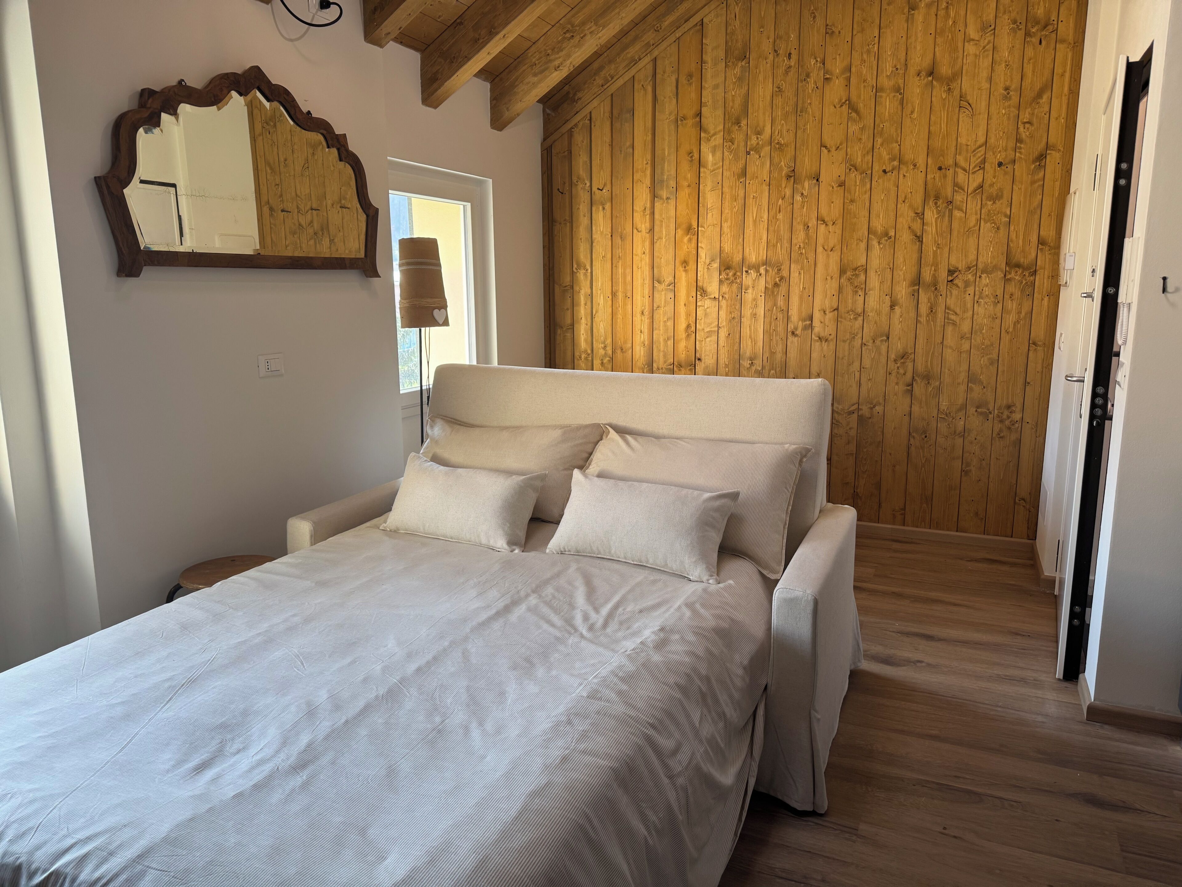 Um quarto com cama, vigas de madeira no teto, painel de parede de madeira e uma janela.