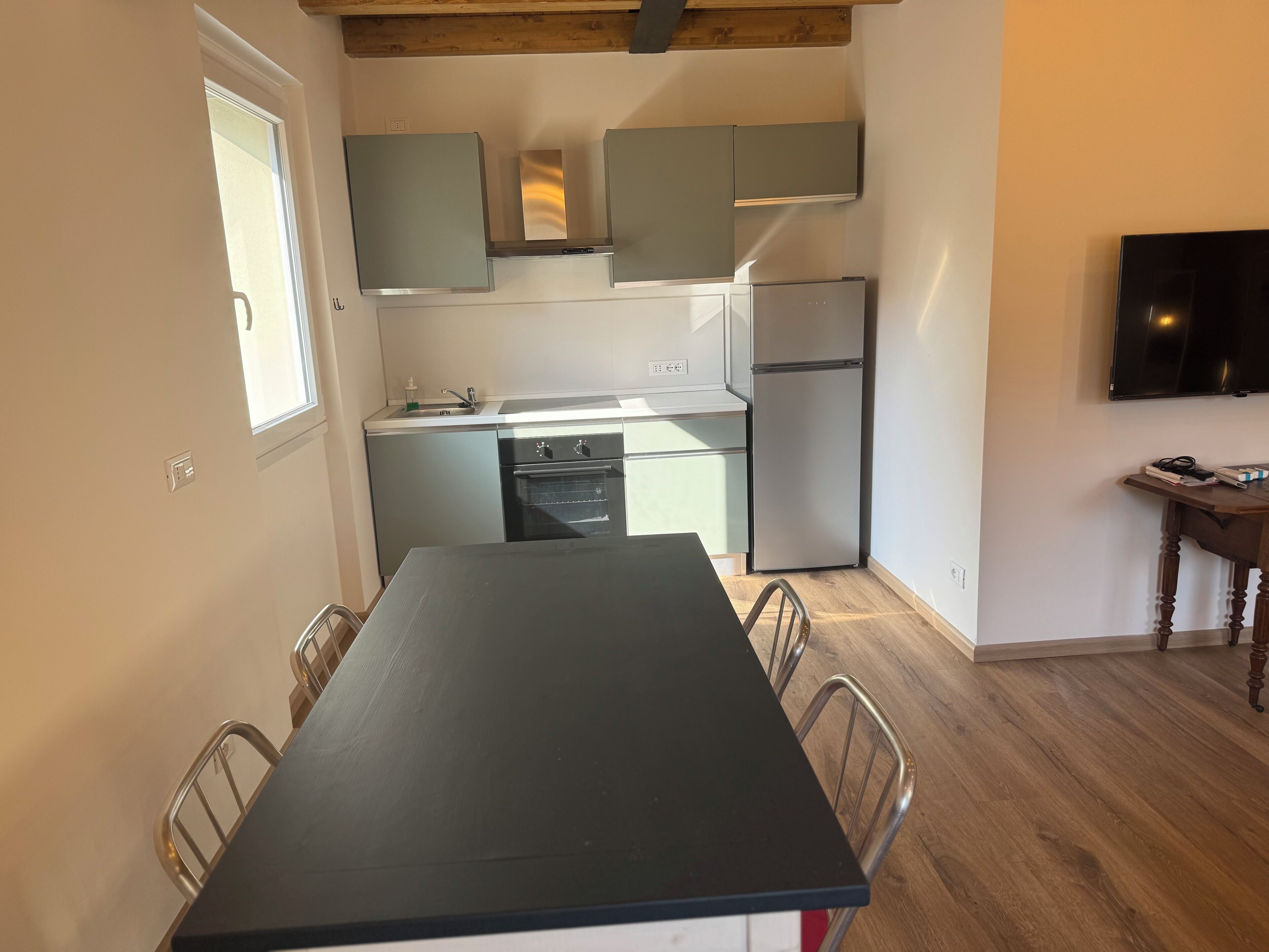 Una cocina compacta con mesa de comedor, electrodomésticos integrados y televisor montado en la pared.