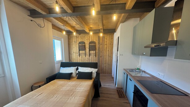Un dormitorio con cama, mesitas de noche, ventana y una kitchenette con pileta y armarios.