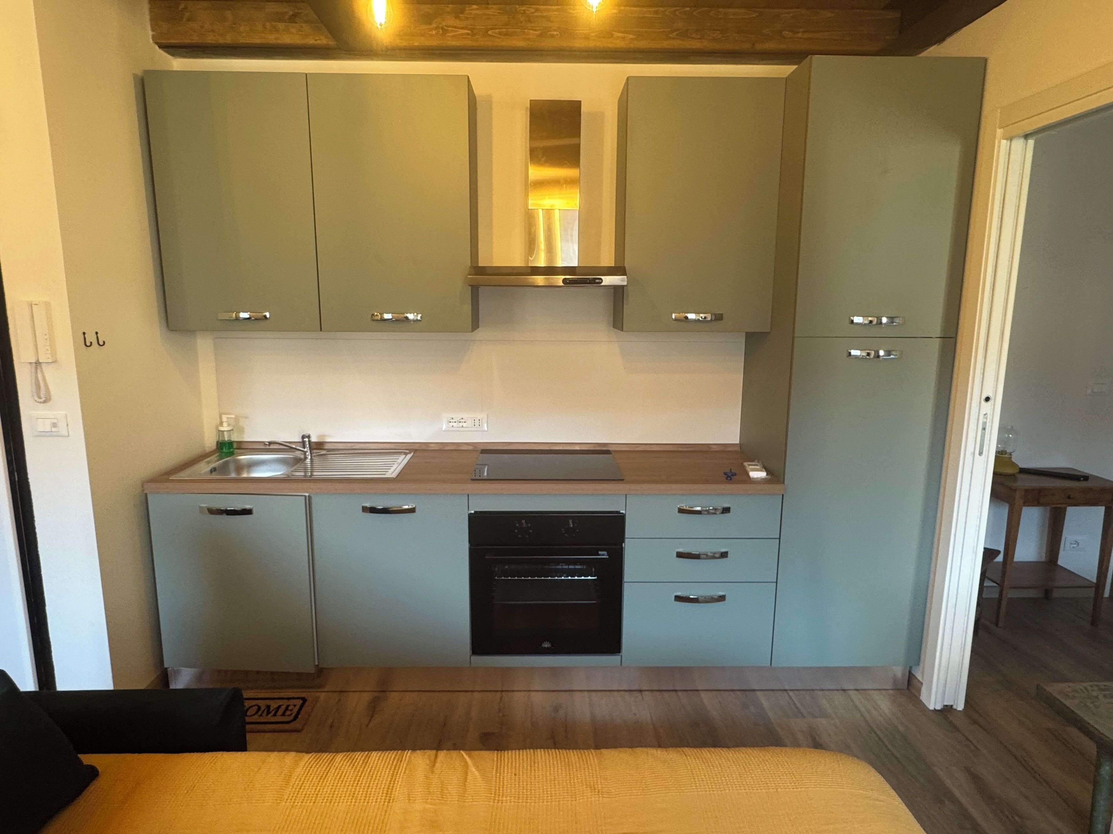 Uma cozinha compacta com armários verde-claros, forno embutido e bancada de madeira.