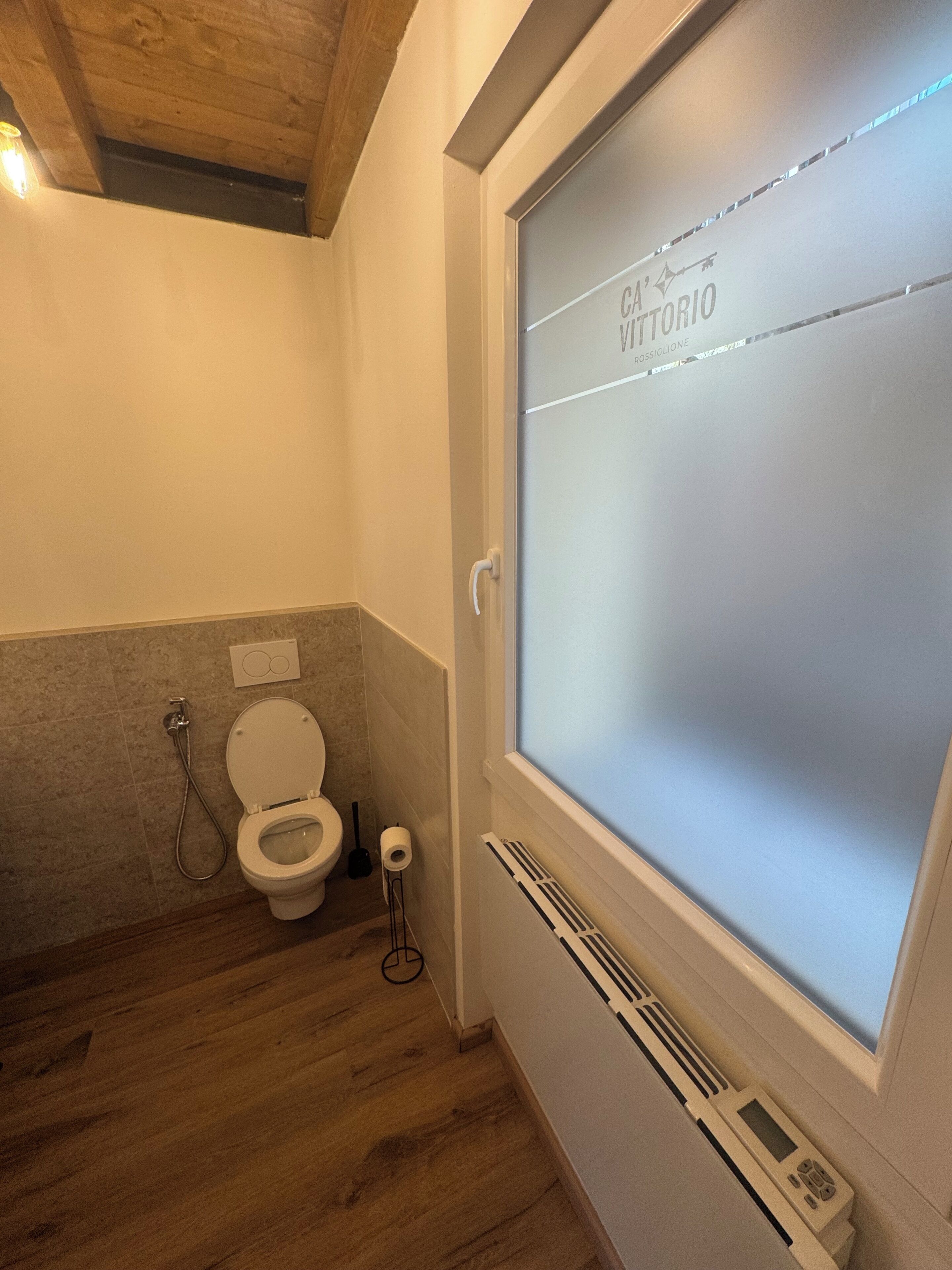 Un baño con inodoro, ducha y ventana con vidrio esmerilado.