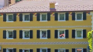 Un edificio amarillo de varios pisos con techo de tejas, numerosas ventanas con contraventanas y un césped bien cuidado al frente.