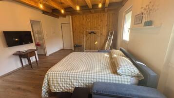 A bedroom with a wooden ceiling, a bed with checkered bedding, a bedside table, a bench, a TV, and a window with a picture frame.