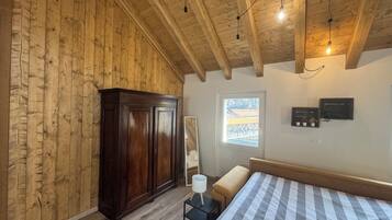 Een slaapkamer met houten wanden, een groot bed, een garderobe, een tafeltje met een lamp en een raam met uitzicht.
